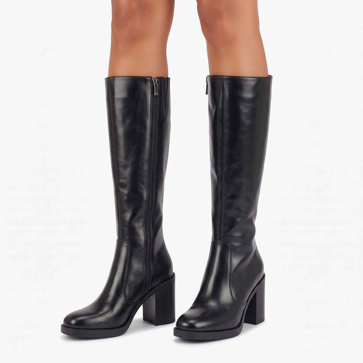 A pair of black knee-high leather boots with block heels and side zippers, shown on a model's feet against a plain white background.
